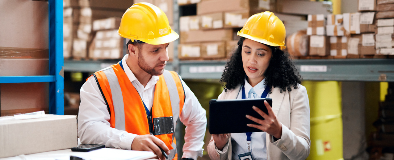 Two people in hard hats reviewing a tablet.